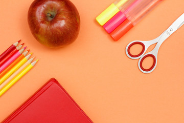 School supplies. Color pencils, book, apple, felt pens and scissors on pink background