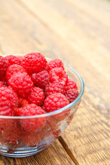 Ripe raspberries in the glass bowl on wooden boards