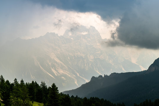  Italian Dolomites landscape. Light after rain in Dolomites. Rocky peaks in the background surrounded by rain clouds. Layers of forest and mountains ridge.  Rocky Mountains Dolomiti. Storm rain over r