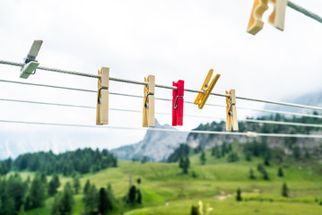 Fototapeta na wymiar Clothes pins on a clothes line rope. clothespins hanging hook. Clothes pins lined up on a wire. Fresh green meadow and mountains on the background. Wooden clothes pins on a string outside laundry