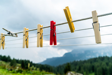 Clothes pins on a clothes line rope. clothespins hanging hook. Clothes pins lined up on a wire. Fresh green meadow and mountains on the background. Wooden clothes pins on a string outside laundry