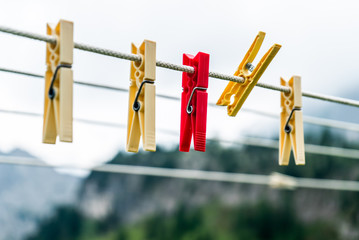 Clothes pins on a clothes line rope. clothespins hanging hook. Clothes pins lined up on a wire. Fresh green meadow and mountains on the background. Wooden clothes pins on a string outside laundry - obrazy, fototapety, plakaty
