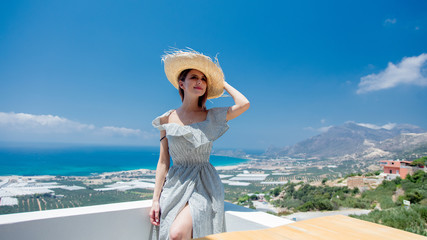 Young woman in white dress and hat is posing on olive garden and sea coast background, Falassandra region, Crete, Greece