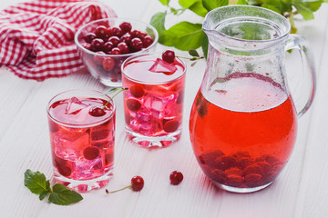 Red cherry cocktail with ice and fresh mint on a white wooden table