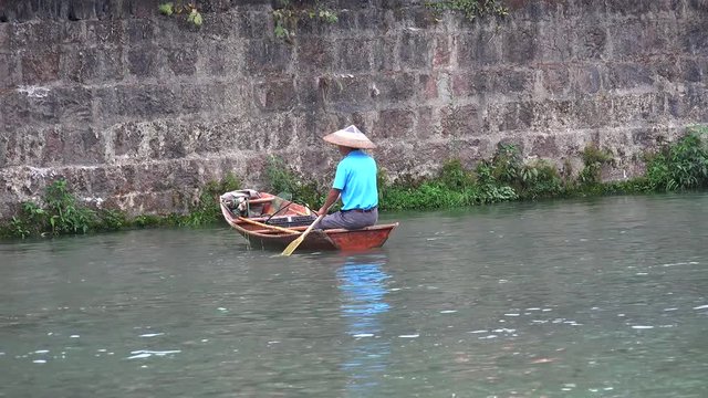 Chinese fisherman in a traditional hat is floating in a boat on the Tuojiang River. Fenghuang, Xiangxi, Hunan, China.