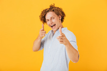 Photo of amusing handsome man 20s smiling and pointing fingers at you, isolated over yellow background