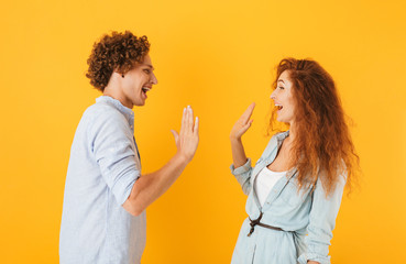 Photo of joyful couple man and woman standing face to face and giving high five, isolated over...