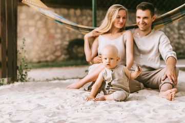 Fototapeta na wymiar smiling family with baby sitting on sand with hammock behind at countryside