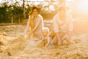 happy parents and little son in linen clothing resting on hay at countryside