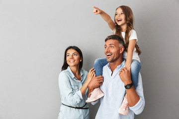Image of european happy family woman and man smiling and looking aside while daughter sitting on the neck of her father, isolated over gray background