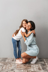 Full length image of happy woman with daughter smiling and hugging together, isolated over gray...