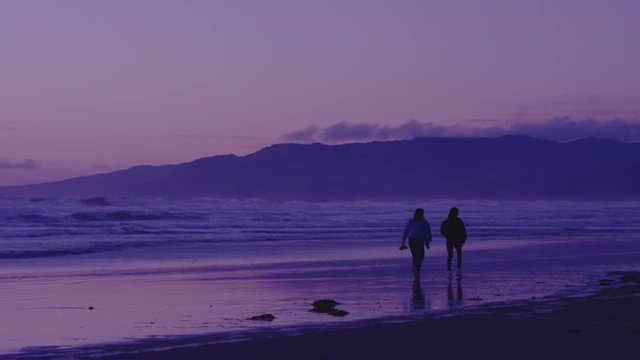 Two female friends enjoying the sunset by walking down the beach at night. Slowmotion. 4K UHD 120fps 16-bit HDR. Shot on RED.