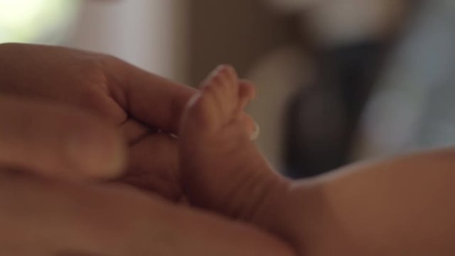 Close-up shot of young loving mother kissing small feet of dear newborn baby