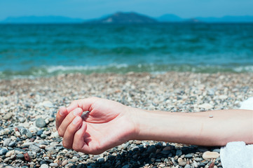 Closeup view of a hand of a man lying on a beach, turquoise sea water in the background. Summer holiday concept