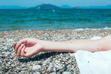 Closeup view of a hand of a man lying on a beach, turquoise sea water in the background. Summer holiday concept