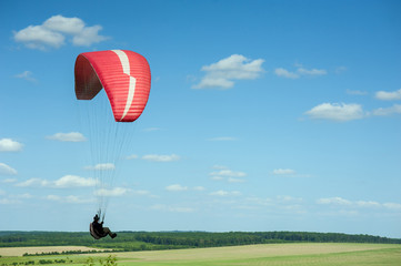 Obraz premium Paragliding over the green field in summer sunny day. One paraglider fly over green field near Dnister river in Ukraine.