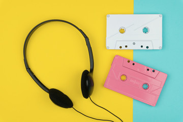 top view of the white and pink audio cassette tapes with the black headphone on yellow and blue background