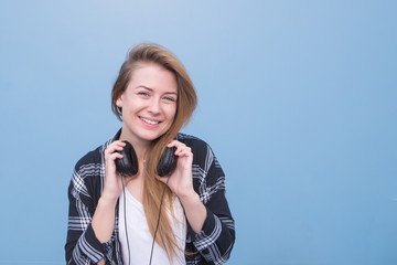 Smiling girl in casual clothing and headphones on the neck on a blue background, looking into the camera and smiling.Copyspace