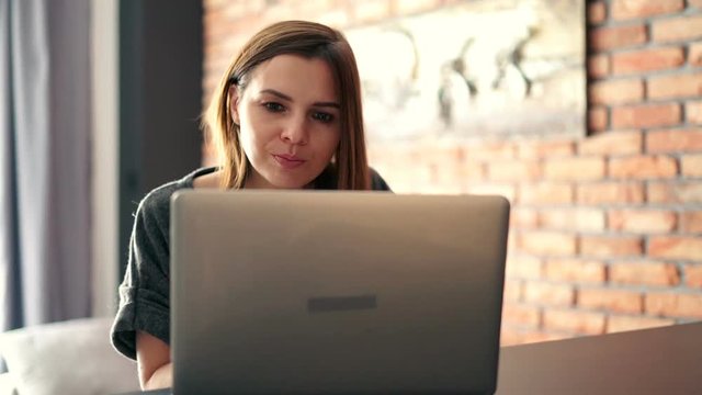 Pretty, young businesswoman working with laptop at home and eating snack
