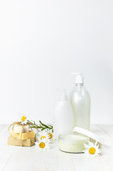 Opened plastic container with cream, handmade soaps, white cosmetic bottle containers and chamomile flower on a white background. Herbal dermatology cosmetic Spa concept organic cosmetic 