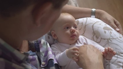 Grandpa babysitting two months old baby granddaughter. He holding child on the lap, looking at her and touching little hands