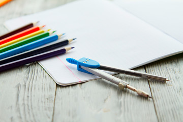 an open notebook on a wooden table lay next to colored pencils and compasses.