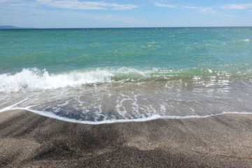 Sea wave with foam passes through a deserted sandy beach.
