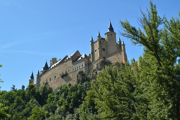 Fototapeta na wymiar Alcazar Castle Seen From The River That Runs Through The Valley That Reigns In Segovia Slightly Caught By A Small Grove. Architecture, Travel, History. June 18, 2018. Segovia Castilla Leon Spain.