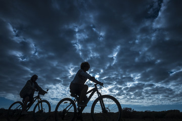 Obraz premium couple of rider in mountain bike come back home after a sport bikes session outdoor. beautiful blue sky with clouds in backgorund. people in silhouette in activity