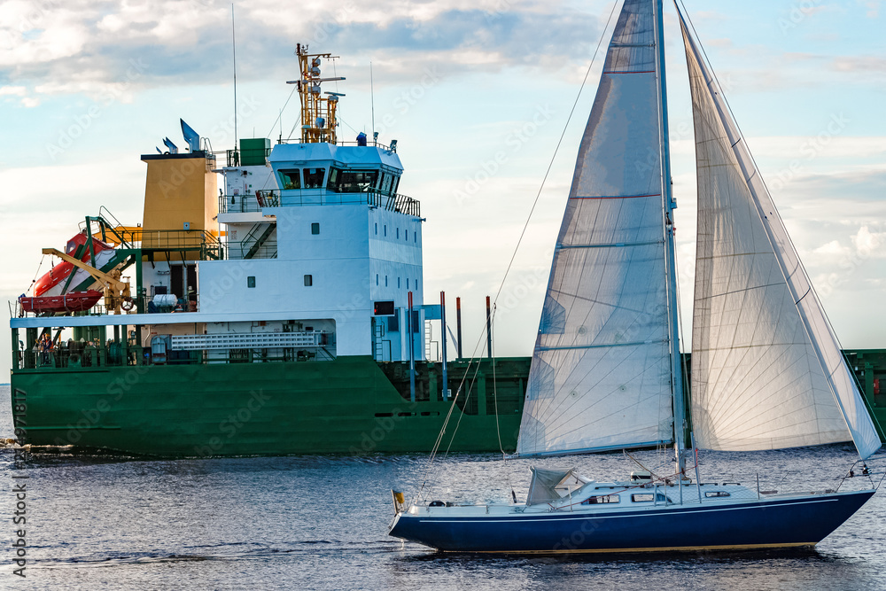 Poster Blue sailboat against cargo ship