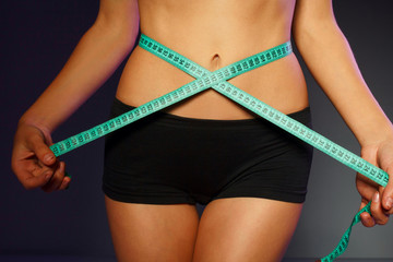 Woman measuring her waist over dark background  with green tape. Wellness concept.