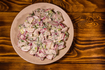 Obraz na płótnie Canvas Vegetarian salad with radish, green onion and sour cream on a ceramic plate. Top view