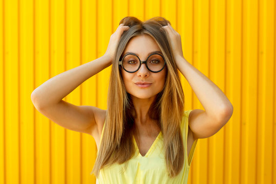 Portrait of a thoughtful girl wearing toy funny glasses looking up over yellow background at daylight