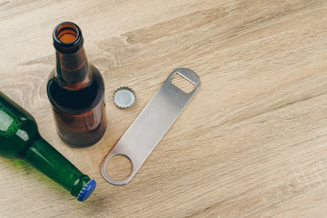 two bottles of beer and a stainless steel bottle opener or bar blade on wooden table - obrazy, fototapety, plakaty