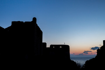 Obraz premium The black silhouette of the Dubrovnik castle tower on sunset with the colorful sky and the dark blue Adriatic Sea, almost clear sky with few small clouds