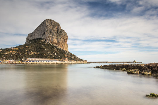 Ifach mountain from water in calm and clouds in the blue sky