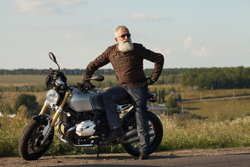 Fototapeta na wymiar Old rider biker man in black leather jacket, jeans, boots and helmet sit on classic style cafe racer motorcycle. Brutal fun urban lifestyle. Outdoor portrait.