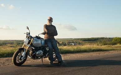 Biker man wearing a leather jacket and sunglasses sitting on his motorcycle.