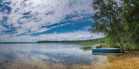 a warm summer day. coast of a beautiful lake with a beach, boats, trees and a sandy bottom under a blue cloudy sky