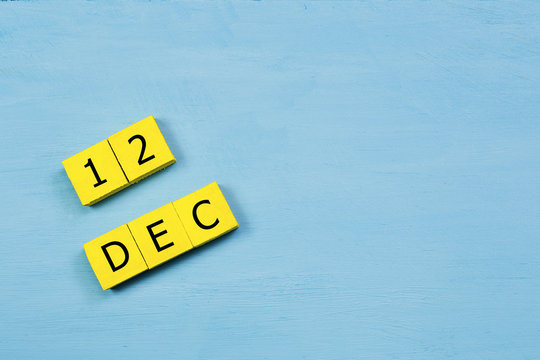 DEC 12, yellow cube calendar on blue wooden surface with copy space