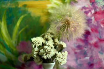 Immortelle flower and dandelion flower in a vase on colorful background.