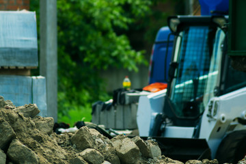 a pile of rubble and soil in the foreground. in the background a mini bulldozer loader and a truck
