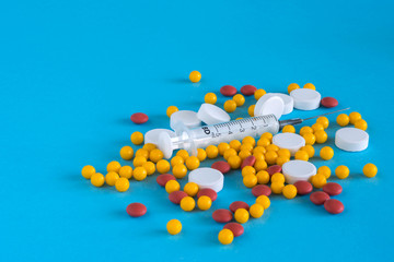 Assorted medical pills, drugs and syringe on blue background, with copy space. Health and medicine