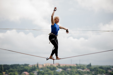 Young woman walking with one arm raised and other to the left on the slackline