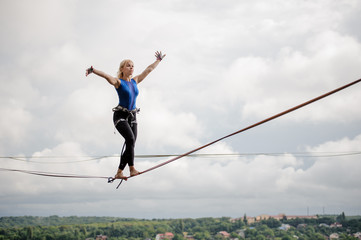 Young smiling woman balancing with arms raised on the slackline rope