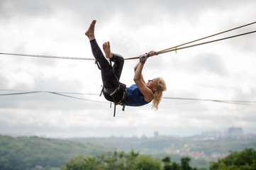 Young woman hanging on the slackline upside down
