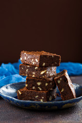 Chocolate brownies with nuts stacked on blue saucer on brown textured tabletop, with blue net fabric, top view