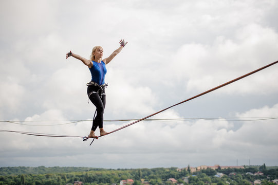 Young smiling woman balancing with arms raised on the slackline rope