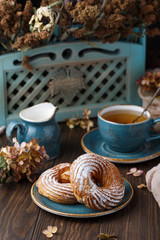 Two curd ring cakes on blue saucer with cup of tea and milk jug, on wooden table, with dried flowers on the background
