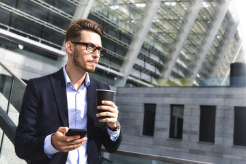 Business man stand at street holding a smartphone and coffee in office park